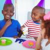 Three young children at a birthday party smiling and wearing party hats